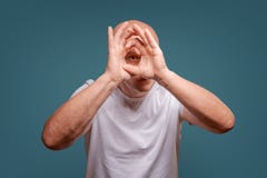 Un hombre en un fondo azul en llevar a cabo las manos cerca de sus ojos como píos de un telescopio imagen de archivo Un hombre en un fondo azul en llevar a cabo las manos cerca de sus ojos como píos de un telescopio imagen de archivo