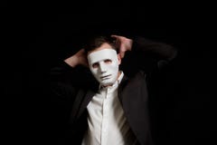 Un hombre en una máscara blanca en un fondo negro abandona Lleva a cabo sus manos detrás de su cabeza imagen de archivo Un hombre en una máscara blanca en un fondo negro abandona Lleva a cabo sus manos detrás de su cabeza imagen de archivo
