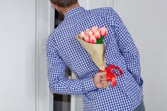 Un hombre joven en una camisa y los vaqueros de tela escocesa azul, refrenando un ramo de tulipanes detrás el suyo, y ojeadas en fotografía de archivo libre de regalías Un hombre joven en una camisa y los vaqueros de tela escocesa azul, refrenando un ramo de tulipanes detrás el suyo, y ojeadas en fotografía de archivo libre de regalías