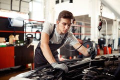 Un hombre joven está ocupado con la comprobación de un motor de automóvil: reparación y mantenimiento del coche foto de archivo libre de regalías Un hombre joven está ocupado con la comprobación de un motor de automóvil: reparación y mantenimiento del coche foto de archivo libre de regalías