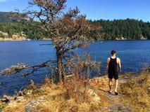 Un hombre joven que camina a lo largo de la trayectoria de la pequeña isla de Alexander que pasa por alto el océano de la bahía d imagen de archivo libre de regalías Un hombre joven que camina a lo largo de la trayectoria de la pequeña isla de Alexander que pasa por alto el océano de la bahía d imagen de archivo libre de regalías