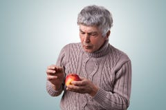 Un hombre maduro con el pelo gris se vistió en el suéter que sostenía una manzana estropeada que lo miraba atento que lo examinab imagen de archivo libre de regalías Un hombre maduro con el pelo gris se vistió en el suéter que sostenía una manzana estropeada que lo miraba atento que lo examinab imagen de archivo libre de regalías