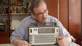 Un hombre mayor con un bigote gira una radio del vintage y escucha la música Saca la antena, gira el botón almacen de metraje de vídeo Un hombre mayor con un bigote gira una radio del vintage y escucha la música Saca la antena, gira el botón almacen de metraje de vídeo