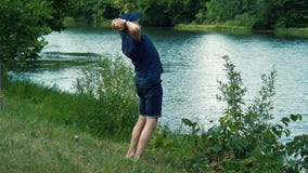 Un homme aux cheveux gris mince dans un T-shirt, un chapeau et des verres bleus marche nu-pieds sur l'herbe verte sur la berge su clips vidéos Un homme aux cheveux gris mince dans un T-shirt, un chapeau et des verres bleus marche nu-pieds sur l'herbe verte sur la berge su clips vidéos