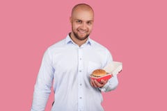 Un homme satisfaisant avec une barbe luxuriante et un chef chauve, tient un hamburger dans sa main et regards à la caméra support photographie stock libre de droits Un homme satisfaisant avec une barbe luxuriante et un chef chauve, tient un hamburger dans sa main et regards à la caméra support photographie stock libre de droits