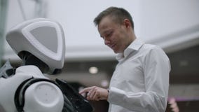Un homme se tient avec un bot de robot et lui pose des questions et demande l'aide en cliquant sur sur l'écran sur le corps de ro banque de vidéos Un homme se tient avec un bot de robot et lui pose des questions et demande l'aide en cliquant sur sur l'écran sur le corps de ro banque de vidéos