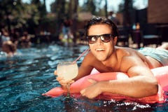 Un individuo en gafas de sol con el cóctel está flotando en un colchón inflable en la piscina fotos de archivo Un individuo en gafas de sol con el cóctel está flotando en un colchón inflable en la piscina fotos de archivo