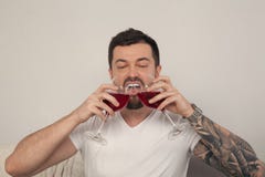Un jeune homme boit du vin de deux verres devant un fond blanc, il est habillé dans un T-shirt blanc photo stock Un jeune homme boit du vin de deux verres devant un fond blanc, il est habillé dans un T-shirt blanc photo stock