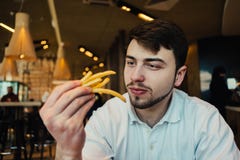 Un jeune homme s'asseyant dans un restaurant et tenant des pommes frites de mains et allant manger photos stock Un jeune homme s'asseyant dans un restaurant et tenant des pommes frites de mains et allant manger photos stock
