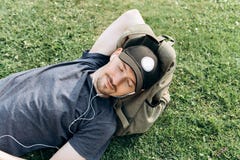 Un jeune type avec un sac à dos se trouve sur l'herbe et écoute la musique images stock Un jeune type avec un sac à dos se trouve sur l'herbe et écoute la musique images stock