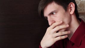 Un jeune type dans une chemise rouge touche ses lèvres avec les doigts de sa main droite, regards de doutes banque de vidéos Un jeune type dans une chemise rouge touche ses lèvres avec les doigts de sa main droite, regards de doutes banque de vidéos