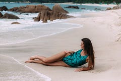 Un modelo zanquilargo, bronceado con el pelo largo oscuro se viste en un traje de baño moderno brillante, aplica una crema que br imagen de archivo libre de regalías Un modelo zanquilargo, bronceado con el pelo largo oscuro se viste en un traje de baño moderno brillante, aplica una crema que br imagen de archivo libre de regalías
