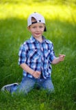 Un niño pequeño en una camisa de tela escocesa azul se está sentando en la hierba verde fotografía de archivo libre de regalías Un niño pequeño en una camisa de tela escocesa azul se está sentando en la hierba verde fotografía de archivo libre de regalías