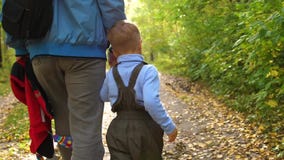 Un padre joven camina en el parque del otoño con su niño El padre lleva a cabo su mano del ` s del hijo Autumn Landscape metrajes Un padre joven camina en el parque del otoño con su niño El padre lleva a cabo su mano del ` s del hijo Autumn Landscape metrajes