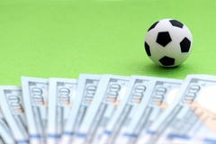 Un pallone da calcio su un campo verde, accanto alle fatture del cento-dollaro degli Stati Uniti Profondità del campo poco profon Immagine Stock Libera da Diritti Un pallone da calcio su un campo verde, accanto alle fatture del cento-dollaro degli Stati Uniti Profondità del campo poco profon Immagine Stock Libera da Diritti