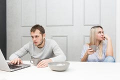 Un par joven está teniendo el hombre del desayuno A trabaja detrás de un ordenador portátil, una mujer aburrida mira al lado fotos de archivo Un par joven está teniendo el hombre del desayuno A trabaja detrás de un ordenador portátil, una mujer aburrida mira al lado fotos de archivo
