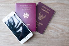 Un pasaporte alemán y pasaporte tailandés con el teléfono móvil blanco en la madera fotos de archivo libres de regalías Un pasaporte alemán y pasaporte tailandés con el teléfono móvil blanco en la madera fotos de archivo libres de regalías
