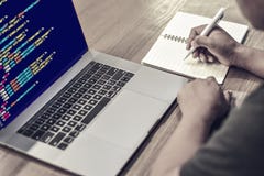 Un programmatore che scrive le note su un taccuino con i codici sorgente di programmazione che visualizzano sullo schermo di un c immagini stock libere da diritti Un programmatore che scrive le note su un taccuino con i codici sorgente di programmazione che visualizzano sullo schermo di un c immagini stock libere da diritti