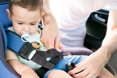 Un père mettant son petit fils dans son siège de voiture Il porte des vêtements décontractés et regarde sa fille Protection dans photo stock Un père mettant son petit fils dans son siège de voiture Il porte des vêtements décontractés et regarde sa fille Protection dans photo stock