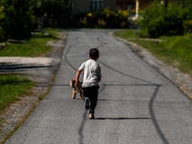 Un ragazzo che corre dopo il suo cane sulla strada cementata di una viuzza in un piccolo villaggio sonnolento fotografia stock libera da diritti Un ragazzo che corre dopo il suo cane sulla strada cementata di una viuzza in un piccolo villaggio sonnolento fotografia stock libera da diritti