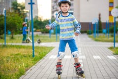 Un ragazzo di due bambini sui pattini di rullo e sul suo fratello del fratello germano sul motorino avvolto in parco Bambini che fotografia stock libera da diritti Un ragazzo di due bambini sui pattini di rullo e sul suo fratello del fratello germano sul motorino avvolto in parco Bambini che fotografia stock libera da diritti