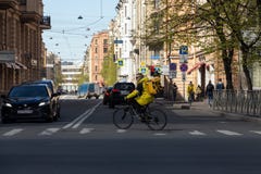 Un repartidor de la comida en una chaqueta amarilla de la marca monta una bicicleta abajo de la comida de Yandex de la calle foto de archivo libre de regalías Un repartidor de la comida en una chaqueta amarilla de la marca monta una bicicleta abajo de la comida de Yandex de la calle foto de archivo libre de regalías