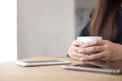 Un ` s de femme remet tenir une tasse de café avec le PC intelligent de téléphone et de comprimé sur la table en bois en café Photos stock Un ` s de femme remet tenir une tasse de café avec le PC intelligent de téléphone et de comprimé sur la table en bois en café Photos stock