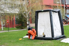 Un sapeur-pompier professionnel dans un costume ignifuge spécial orange dispose à assembler une tente blanche de l'oxygène aux pe image stock Un sapeur-pompier professionnel dans un costume ignifuge spécial orange dispose à assembler une tente blanche de l'oxygène aux pe image stock