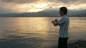 Un uomo in una camicia controlla i messaggi sull'orologio astuto durante l'alba sulla spiaggia dell'oceano e delle montagne C'è u archivi video Un uomo in una camicia controlla i messaggi sull'orologio astuto durante l'alba sulla spiaggia dell'oceano e delle montagne C'è u archivi video