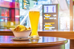 Un vetro di birra e di un piatto del pangrattato e del formaggio Nei precedenti, il bordo online visualizza i voli all'aeroporto immagine stock libera da diritti Un vetro di birra e di un piatto del pangrattato e del formaggio Nei precedenti, il bordo online visualizza i voli all'aeroporto immagine stock libera da diritti