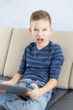 Un écolier joue un jeu vidéo sur la tablette, montrant la colère et l'agression photographie stock libre de droits Un écolier joue un jeu vidéo sur la tablette, montrant la colère et l'agression photographie stock libre de droits