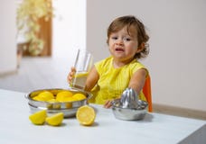 Una bambina in un vestito giallo assaggia la limonata cucinata immagini stock libere da diritti Una bambina in un vestito giallo assaggia la limonata cucinata immagini stock libere da diritti