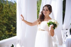 Una bella giovane sposa che porta un abito di nozze bianco come la neve sta camminando su un terrazzo aperto decorato con le tend fotografia stock Una bella giovane sposa che porta un abito di nozze bianco come la neve sta camminando su un terrazzo aperto decorato con le tend fotografia stock