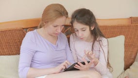 Una bella madre e la sua piccola conversazione della figlia bene, la madre tiene una compressa ed insegna a sua figlia stock footage Una bella madre e la sua piccola conversazione della figlia bene, la madre tiene una compressa ed insegna a sua figlia stock footage