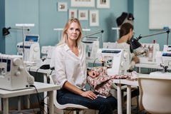 Una camicia bianca d'uso della donna bionda graziosa Smart di aspetto sta cucendo con la cucire-macchina elettrica Modo, sarto fotografia stock libera da diritti Una camicia bianca d'uso della donna bionda graziosa Smart di aspetto sta cucendo con la cucire-macchina elettrica Modo, sarto fotografia stock libera da diritti
