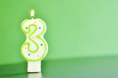 Una candela accesa che rappresenta figura tre, 3 di cifra, su fondo verde con lo spazio della copia fotografia stock libera da diritti Una candela accesa che rappresenta figura tre, 3 di cifra, su fondo verde con lo spazio della copia fotografia stock libera da diritti