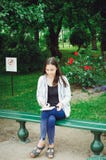 Una chica joven se sienta en un banco en el jardín y dibuja fotografía de archivo libre de regalías Una chica joven se sienta en un banco en el jardín y dibuja fotografía de archivo libre de regalías
