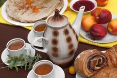 Una composizione all'aperto con le tazze di tè, una teiera, un piatto dei pancake, una pasticceria, una frutta matura ed il campo immagine stock libera da diritti Una composizione all'aperto con le tazze di tè, una teiera, un piatto dei pancake, una pasticceria, una frutta matura ed il campo immagine stock libera da diritti