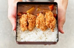 Una femmina utilizza le mani alla tenuta ed a passare del piatto della guarnizione giapponese del riso di curry con il pollo frit fotografie stock libere da diritti Una femmina utilizza le mani alla tenuta ed a passare del piatto della guarnizione giapponese del riso di curry con il pollo frit fotografie stock libere da diritti