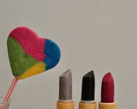 Una fila de los palillos de labio exhibidos con una piruleta colorida de la forma del corazón Imagen de archivo libre de regalías Una fila de los palillos de labio exhibidos con una piruleta colorida de la forma del corazón Imagen de archivo libre de regalías