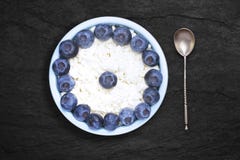 Una foto sopraelevata della ricotta naturale fresca con i mirtilli e un cucchiaio d'argento in una ciotola ceramica sullo scritto fotografie stock libere da diritti Una foto sopraelevata della ricotta naturale fresca con i mirtilli e un cucchiaio d'argento in una ciotola ceramica sullo scritto fotografie stock libere da diritti