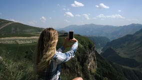 Una giovane ragazza bionda si siede sull'erba su un fondo delle montagne con uno zaino e prende le immagini delle montagne archivi video Una giovane ragazza bionda si siede sull'erba su un fondo delle montagne con uno zaino e prende le immagini delle montagne archivi video