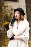 Una giovane signora in un black hat e guanti e un cappotto leggero sta e guarda esteriormente retro all'aperto fotografia stock Una giovane signora in un black hat e guanti e un cappotto leggero sta e guarda esteriormente retro all'aperto fotografia stock