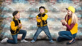 Una madre giovane e due giovani figli nello stile di hip-hop Famiglia alla moda Graffiti sulle pareti immagine stock libera da diritti Una madre giovane e due giovani figli nello stile di hip-hop Famiglia alla moda Graffiti sulle pareti immagine stock libera da diritti