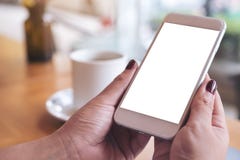 Una mano del ` s de la mujer que sostiene el teléfono móvil blanco con la taza de escritorio en blanco de la pantalla y de café e imágenes de archivo libres de regalías Una mano del ` s de la mujer que sostiene el teléfono móvil blanco con la taza de escritorio en blanco de la pantalla y de café e imágenes de archivo libres de regalías