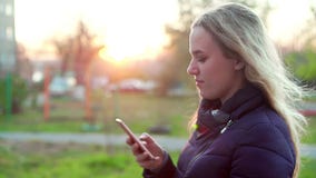 Una muchacha atractiva joven se está colocando en la calle con un smartphone en su mano almacen de metraje de vídeo Una muchacha atractiva joven se está colocando en la calle con un smartphone en su mano almacen de metraje de vídeo