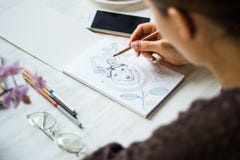 Una muchacha está pintando con los lápices fornido en una hoja blanca en un café en un fondo de madera blanco de la luz de la tab fotos de archivo Una muchacha está pintando con los lápices fornido en una hoja blanca en un café en un fondo de madera blanco de la luz de la tab fotos de archivo