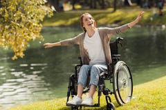 Una mujer en una silla de ruedas se sienta en la orilla de un lago Ella se separó los brazos hacia fuera y rió imagen de archivo libre de regalías Una mujer en una silla de ruedas se sienta en la orilla de un lago Ella se separó los brazos hacia fuera y rió imagen de archivo libre de regalías