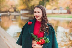 Una mujer joven camina en el parque del otoño Mujer morena que lleva una capa verde y un vestido rojo imágenes de archivo libres de regalías Una mujer joven camina en el parque del otoño Mujer morena que lleva una capa verde y un vestido rojo imágenes de archivo libres de regalías