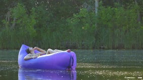 Una mujer joven que miente en un colchón neumático toma tomar el sol y navega a lo largo del río metrajes Una mujer joven que miente en un colchón neumático toma tomar el sol y navega a lo largo del río metrajes